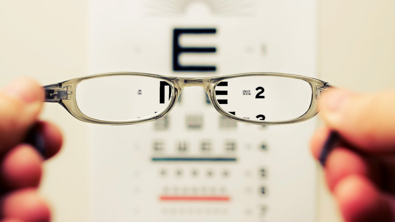 Óculos e, no fundo, parede com várias letras desfocadas