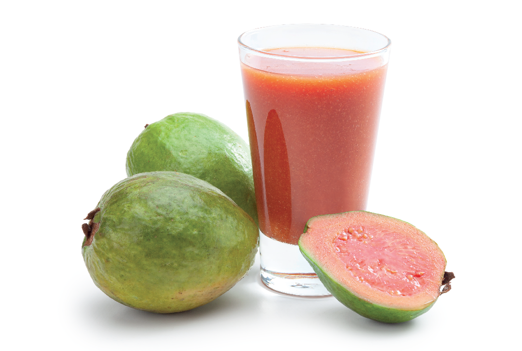 Um copo de suco de goiaba rosa ao lado de duas goiabas verdes inteiras e uma goiaba verde cortada ao meio, revelando sua polpa rosa com sementes, tudo sobre fundo branco