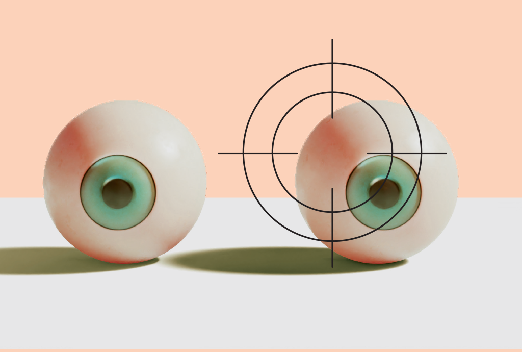 Dois globos oculares artificiais com íris verde-azulada e esclera esbranquiçada, um deles com mira de alvo sobreposta, em fundo pêssego e base cinza claro
